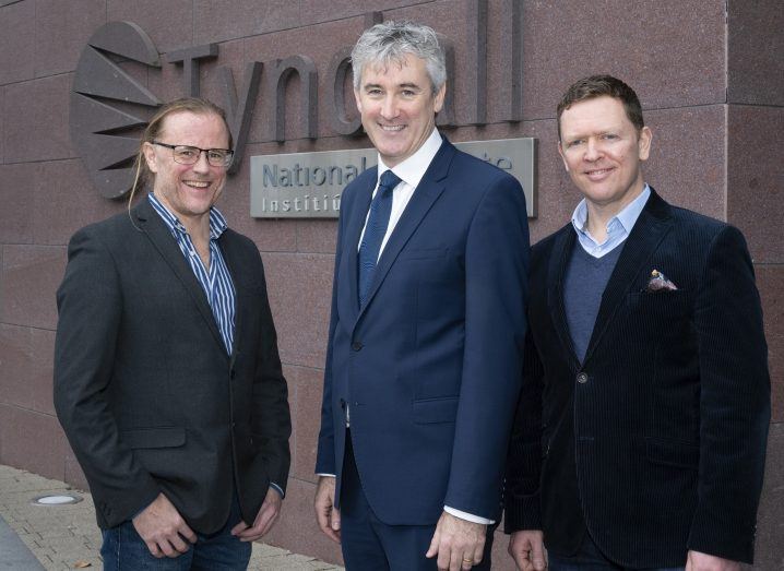 Three men wearing suits stand next to each other and smile.