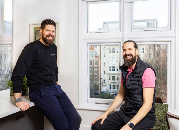 Two men smile for a photograph from inside an office space.