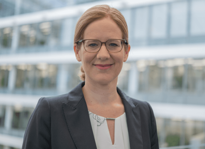 A woman wearing business attire and glasses smiles at the camera with a blurred office building behind her. She is Sabine Erlinghagen, CEO of Siemens Grid Software.