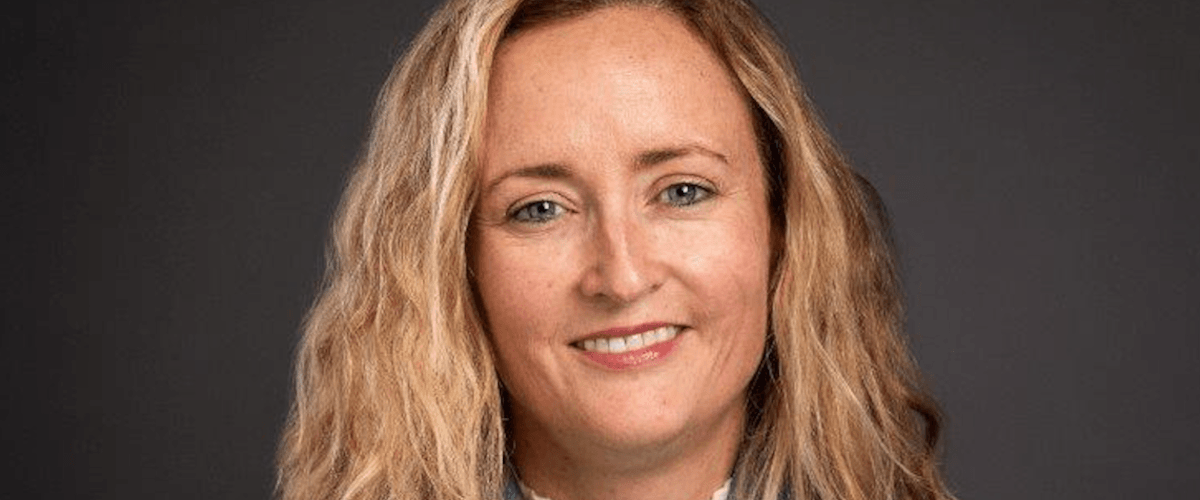 A woman with blonde hair smiles in front of a dark grey background. She is Sinéad Bailey, country lead for Ireland at Bristol Myers Squibb.