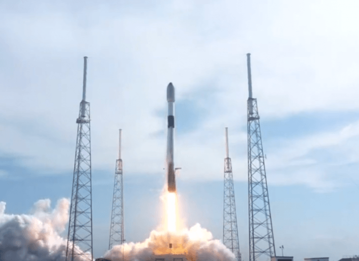 A SpaceX Falcon 9 rocket taking off into the sky from a launch station, with a jet of fire under it.